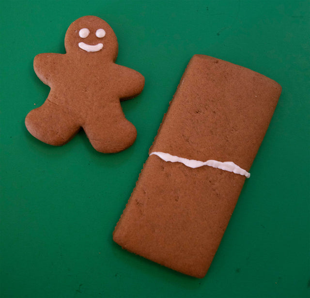 A smiling gingerbread man next to a square of gingerbread, which is split in half and repaired with white frosting.